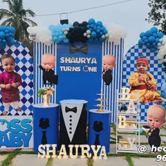A sharp and stylish Boss Baby theme for a first birthday. The setup includes multiple character cutouts, a striped and checkered backdrop, and plinths decorated with tuxedo and tie graphics.