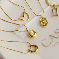 A collection of minimalist gold pendants and necklaces arranged on a branded plate. This clean, organized flatlay is excellent for showcasing the variety within a product line.