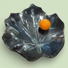 Another view of the large, leaf-shaped platter, showing how the glaze pools and breaks over the texture. The single orange provides a sense of scale for this unique, nature-inspired centerpiece.