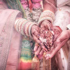 A close-up shot of a wedding ritual, focusing on the couple's hands. This detailed photograph highlights the bride's intricate mehndi and the symbolic actions that unite them.