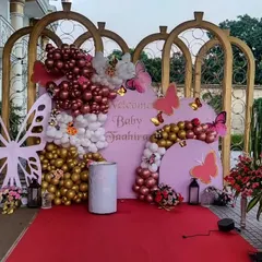 A beautiful butterfly-themed welcome party for baby Jaahira. This outdoor setup includes elegant golden arches, a personalized backdrop, and a mix of chrome, pastel, and white balloons for a sophisticated look.