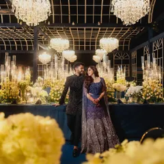 A quiet moment for the couple amidst the grandeur of their reception. The deep blue decor, crystal chandeliers, and endless candles create a cinematic and romantic atmosphere, perfectly captured in this portrait.