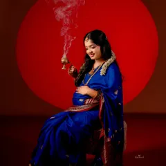 A striking portrait featuring a mom-to-be in a royal blue saree, holding a traditional incense burner. The bold red circular background adds a modern, graphic element to this cultural shot.