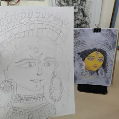 This image shows the process of learning to draw from a reference. On the right is the reference photo of Durga, and on the left is a student's pencil sketch, capturing the facial features and ornaments.