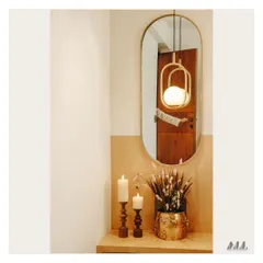 A simple yet elegant corner vignette. The composition of a modern pendant light, an oval mirror, and classic candle holders creates a warm and welcoming ambiance.
