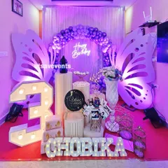 A beautiful butterfly-themed birthday in shades of purple and white. This indoor setup includes large butterfly wing cutouts, a marquee number '3', and a neon sign, perfect for a magical celebration.