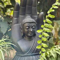 Our black marble Buddha in a blessing hand sculpture, seen here nestled among ferns, adds a touch of serenity and botanical styling to any corner.