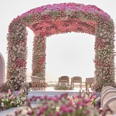 A closer look at the beachside mandap, where the couple took their vows. The structure is completely covered in thousands of pink and white flowers, creating a soft, romantic canopy against the bright sky.