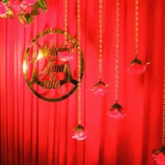 Detail of the personalized gold acrylic hoop sign, hanging against the red backdrop with delicate floral strings. These custom signs are a popular choice for roka and engagement ceremonies.