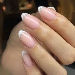 A modern twist on a classic. This elegant French manicure on almond-shaped nails is elevated with a tiny, delicate pearl accent at the base of each tip, adding a touch of sophisticated detail.