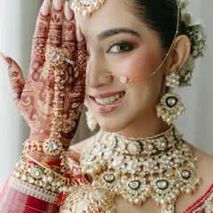 A beautiful close-up of the bride, her hand with intricate henna art partially covering her smiling face.