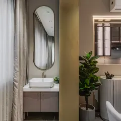 This exquisite basin area features a sculptural oval mirror that gracefully elongates the space, while the floating vanity in muted taupe exudes understated elegance. The seamless integration of a minimalist vessel sink and brushed gold faucet transforms this corner into a statement of sophisticated serenity.