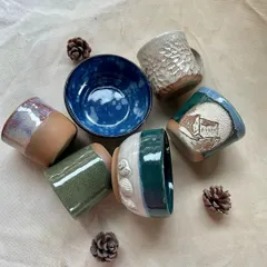 A collection of colorful, glazed mugs and bowls created by students. Each piece is unique, showcasing different glazing techniques, textures, and hand-carved details.
