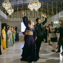 A full-length shot of the couple's energetic entrance at their Sangeet celebration, with guests cheering them on.