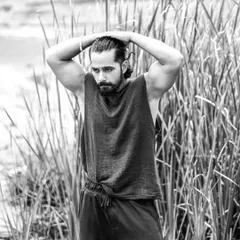 A black and white portrait of an actor in a natural, outdoor setting. The focus is on his strong physique and intense expression, creating a raw and powerful image.