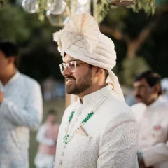 A candid shot of the groom smiling during the wedding ceremony, looking dapper in his all-white sherwani and safa.