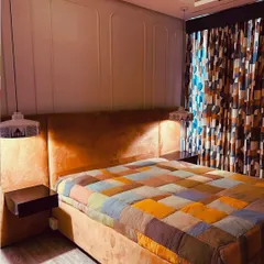 We infused this bedroom with personality and warmth. The custom bed and headboard in a vibrant orange fabric are the focal point, complemented by sleek floating side tables and unique skyline-printed pendant lights. The wall features subtle wainscoting for a classic touch.