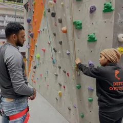 An instructor explains the basics of our auto belay system to a new climber. This system allows you to climb on your own and descend safely, making it perfect for practice.