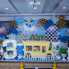 The full stage view for Shriyansh's 3rd birthday party. You can see the large marquee '3', the Cocomelon bus dessert table, and the coordinated balloon garlands that frame the entire setup.