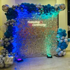 The sequin wall backdrop for the naming ceremony, shown here with a mix of blue and green lighting. The silver and blue balloon frame completes the modern look.