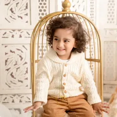 A candid shot of a smiling toddler seated in a stylish golden chair prop. My goal is to capture genuine expressions and playful moments.