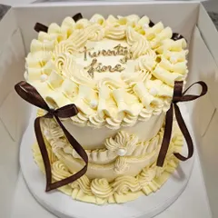A beautiful off-white vintage cake with intricate buttercream piping and delicate chocolate-brown ribbons. This style, often called Lambeth piping, involves creating layers of detailed scrollwork and shells.