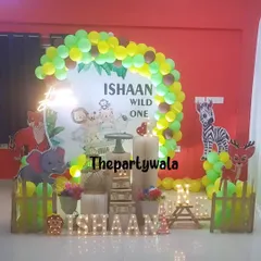 A bright and cheerful jungle theme for a 'Wild One' birthday. The setup includes a neon sign and cutouts of a tiger, elephant, and zebra.