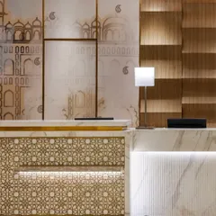 A detailed view of the reception desk, highlighting the intricate geometric pattern on its facade. This bespoke element, combined with the clean lines of the marble and warm backlighting, creates a refined and memorable first impression.
