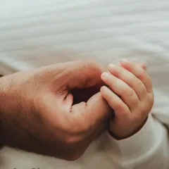 A father's hand gently holding his baby's tiny hand. This simple, close-up shot is full of warmth and connection.
