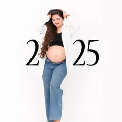 A modern and casual maternity portrait against a clean white background. The mom-to-be is styled in jeans and a crop top, creating a fresh and contemporary look for a 2025 due date announcement.