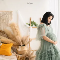 The soft green gown blends beautifully with the natural light and bohemian decor of the studio, creating a peaceful and dreamy portrait by the window.