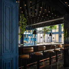 The bar area is detailed with classic retro elements, including brown leather bar stools with brass footrests and a carefully lit back bar. The dark, reflective surfaces and patterned wall panels contribute to a sophisticated and indulgent atmosphere.