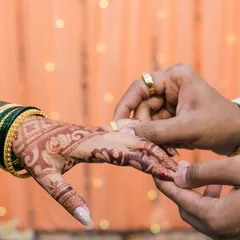 A macro shot of the ring exchange, focusing on the hands, the ring, and the bride's intricate henna. This highlights a key moment of the engagement ceremony.