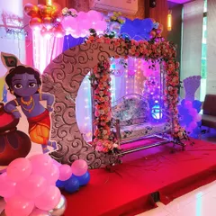 A baby shower setup featuring a decorated cradle, a floral moon arch, and a cutout of little Krishna.