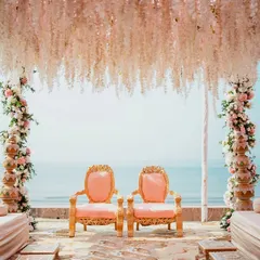 A serene shot of the beachside wedding mandap before the ceremony begins. The elegant chairs, floral arrangements, and the ocean backdrop create a sense of peaceful anticipation.