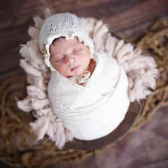 A precious newborn wrapped snugly in a white bonnet and swaddle, resting in a rustic bowl. I provide all the props for a safe and beautiful newborn session.