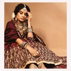 The complete look for our vintage-inspired bride. The heavily embroidered lehenga in a deep maroon, paired with layers of antique-finish jewelry and a fresh flower in her hair, creates a look that is both opulent and timeless.
