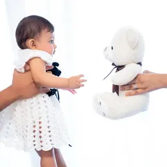 A side profile of the baby reaching for her teddy bear. The high-key lighting and white background create a clean, modern, and airy feel for this baby portrait.