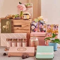 This pastel-themed festive arrangement shows a softer aesthetic, with floral gift boxes, a live orchid plant, gourmet jam, and other delicate treats packed into a stylish wooden crate.
