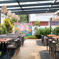 The outdoor space at Pink Verranda is anchored by a vibrant, hand-painted floral mural, adding a burst of color and artistry. This area combines comfortable seating with natural elements to feel like a garden oasis in the city.