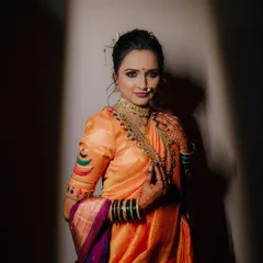 A full-length bridal portrait using dramatic lighting to create a spotlight effect, making the bride and her stunning orange saree the absolute focus.