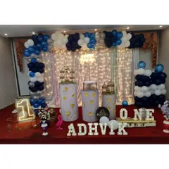 A full stage setup for a first birthday, featuring a balloon backdrop, light-up letters, and a neon number '1'.