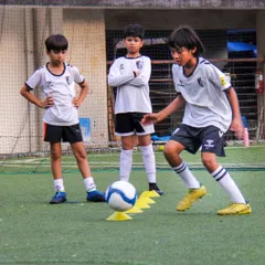 An older player demonstrates a complex dribbling drill while his teammates observe. Peer learning is a key part of our advanced team culture.