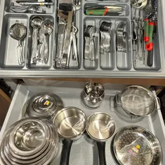 A complete drawer system for an Indian kitchen. The top drawer is for cutlery and tools, while the bottom holds steel tiffins, bowls, and serving spoons, all neatly arranged.