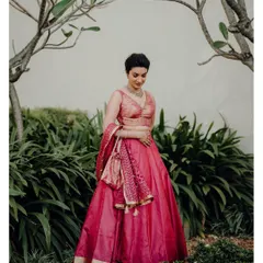 A full-length portrait of Jisha in her elegant pink lehenga, set in a beautiful garden.