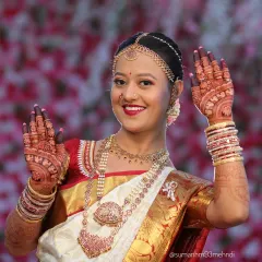 A radiant bride showcasing her full wedding look. Her detailed mehndi complements her jewelry and saree, completing her stunning bridal appearance.