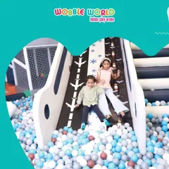 Two girls sliding down our runway-themed slide straight into the ball pit. It's all about playing hard and having a blast.