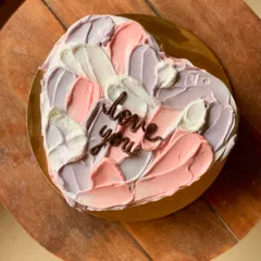 A heart-shaped cake with abstract pastel buttercream strokes and a simple "love you" message. This artistic design is modern and romantic.