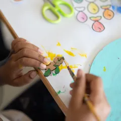 A close-up of tiny hands painting a small wooden cutout. In my classes, I focus on the process, encouraging kids to explore different brush strokes and color combinations. Every detail is a step in their creative journey.