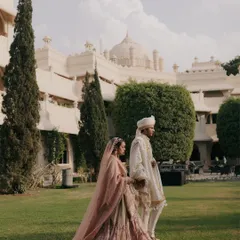 A cinematic portrait of Apurva and Hemant walking through the lush gardens of a heritage property in Jaipur, their pastel outfits complementing the serene environment.